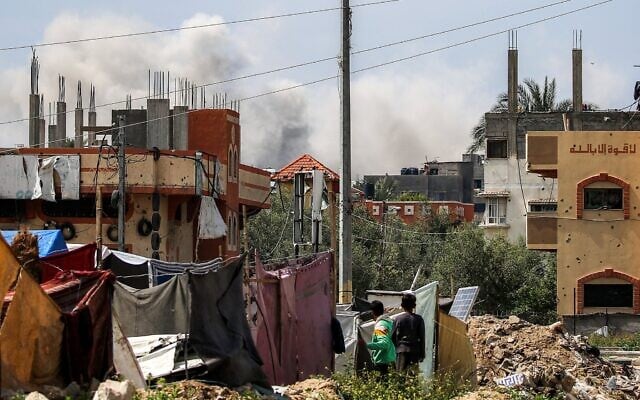 Des garçons debout à côté d'abris de fortune regardent un panache de fumée s'élever d'un bâtiment touché par un bombardement israélien après un avertissement préalable dans le camp de réfugiés palestiniens de Nuseirat, dans le centre de la bande de Gaza, le 25 mars 2025. (Crédit : Eyad BABA / AFP) Des garçons debout à côté d'abris de fortune regardent un panache de fumée s'élever d'un bâtiment touché par un bombardement israélien après un avertissement préalable dans le camp de réfugiés palestiniens de Nuseirat, dans le centre de la bande de Gaza, le 25 mars 2025. (Crédit : Eyad BABA / AFP)