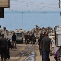Un bateau de la marine israélienne naviguant au large de la ville de Gaza en mer Méditerranée alors que des civils marchent dans une allée du bord de mer, le 28 mars 2025. (Crédit : Omar al-Qattaa/AFP)