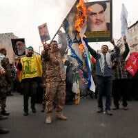 Des manifestants iraniens brûlent un drapeau israélien alors qu'ils brandissent des affiches du défunt fondateur de la révolution iranienne, l'ayatollah Khomeini, et du guide suprême, l'ayatollah Ali Khamenei, lors du rassemblement annuel de la Journée de Jérusalem ou Journée de Qods contre Israël, à Téhéran, en Iran, le 28 mars 2025. (Crédit : AP/Vahid Salemi)