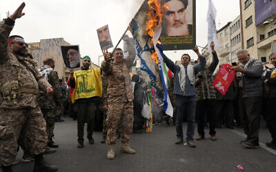 Des manifestants iraniens brûlent un drapeau israélien alors qu'ils brandissent des affiches du défunt fondateur de la révolution iranienne, l'ayatollah Khomeini, et du guide suprême, l'ayatollah Ali Khamenei, lors du rassemblement annuel de la Journée de Jérusalem ou Journée de Qods contre Israël, à Téhéran, en Iran, le 28 mars 2025. (Crédit : AP/Vahid Salemi)