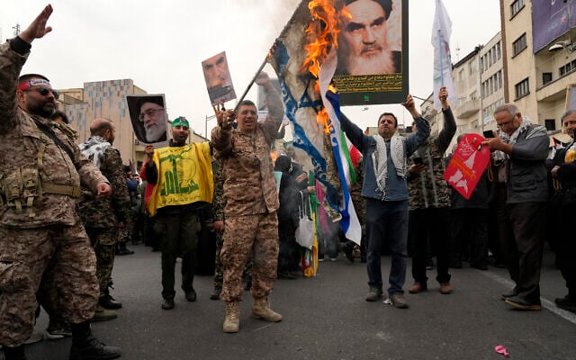 Des manifestants iraniens brûlent un drapeau israélien alors qu'ils brandissent des affiches du défunt fondateur de la révolution iranienne, l'ayatollah Khomeini, et du guide suprême, l'ayatollah Ali Khamenei, lors du rassemblement annuel de la Journée de Jérusalem ou Journée de Qods contre Israël, à Téhéran, en Iran, le 28 mars 2025. (Crédit : AP/Vahid Salemi)