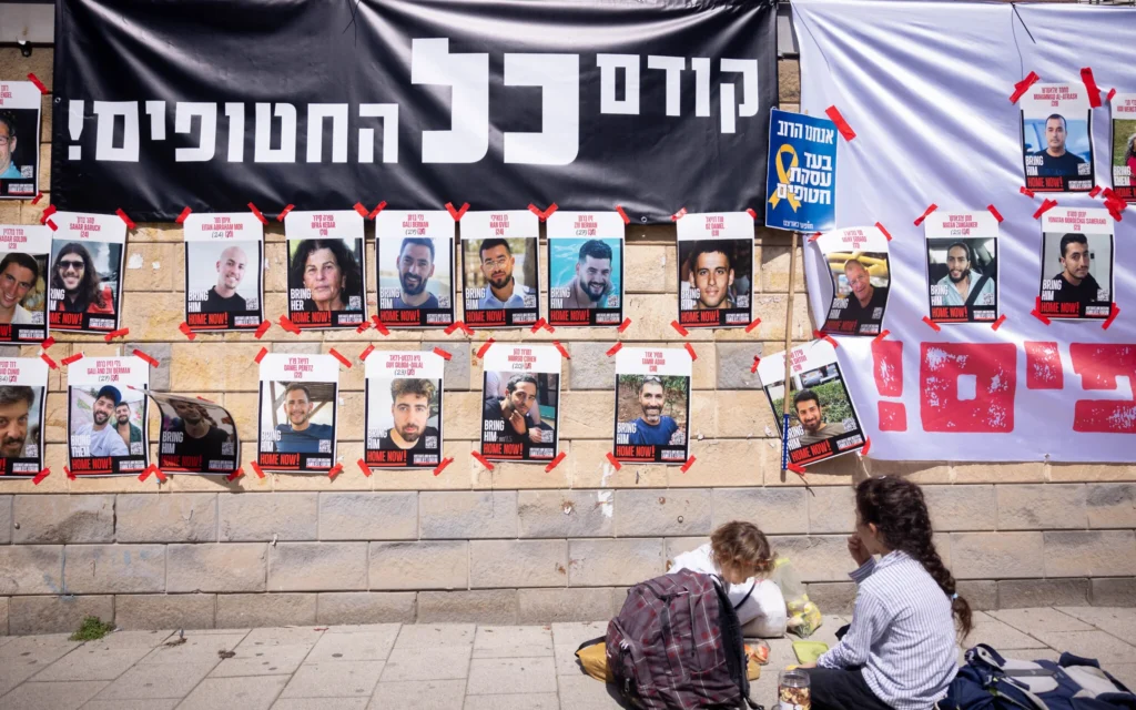 Des affiches d'Israéliens otages à Gaza devant le ministère de la Défense à Tel Aviv, sous une banderole indiquant : « Les otages avant tout! » le 9 mars 2025. (Crédit : Miriam Alster/FLASH90)