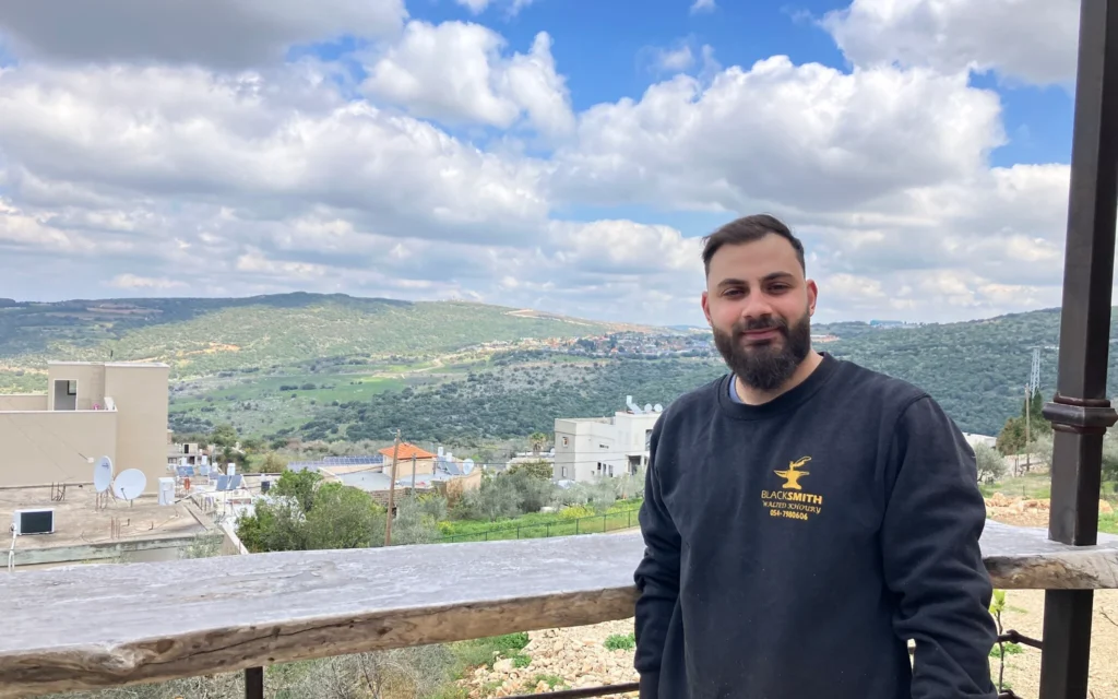 Khalil Khoury se tient sur le porche de sa maison avec le Liban en arrière-plan, le 23 mars 2025. (Crédit : Diana Bletter/Times of Israel)