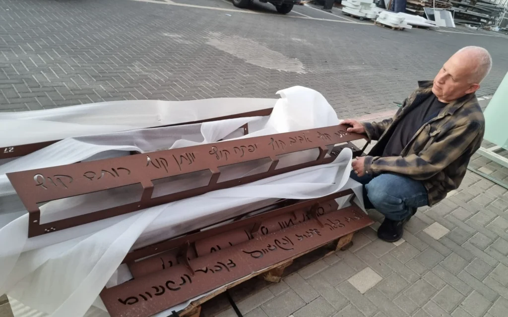 L'architecte Zvika Pasternak avec quelques-unes des bandes en métal sur lesquelles sont inscrites les signatures des 64 résidents assassinés au kibboutz Kfar Aza par des terroristes du Hamas le 7 octobre 2023. (Crédit : Zvika Pasternak) L'architecte Zvika Pasternak avec quelques-unes des bandes en métal sur lesquelles sont inscrites les signatures des 64 résidents assassinés au kibboutz Kfar Aza par des terroristes du Hamas le 7 octobre 2023. (Crédit : Zvika Pasternak)