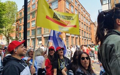 Des personnes regardent les coureurs du marathon de Londres et tiennent une grande banderole appelant au retour des otages détenus par le groupe terroriste palestinien du Hamas à Gaza, le 27 avril 2025. (Crédit : Forum des familles d’otages et de disparus)