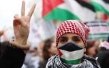 Illustration : Une manifestante portant un masque aux couleurs palestiniennes et un keffieh faisant le signe de la victoire lors d'une manifestation appelant à un cessez-le-feu immédiat dans la bande de Gaza, sur la place de la République, à Paris, le 9 mars 2024. (Crédit : Emmanuel Dunand/AFP)