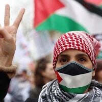 Illustration : Une manifestante portant un masque aux couleurs palestiniennes et un keffieh faisant le signe de la victoire lors d'une manifestation appelant à un cessez-le-feu immédiat dans la bande de Gaza, sur la place de la République, à Paris, le 9 mars 2024. (Crédit : Emmanuel Dunand/AFP)