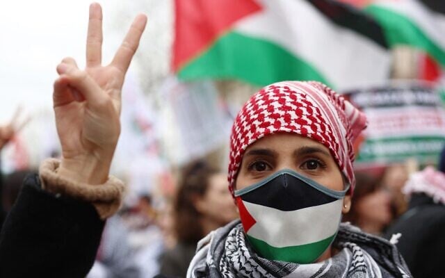 Illustration : Une manifestante portant un masque aux couleurs palestiniennes et un keffieh faisant le signe de la victoire lors d'une manifestation appelant à un cessez-le-feu immédiat dans la bande de Gaza, sur la place de la République, à Paris, le 9 mars 2024. (Crédit : Emmanuel Dunand/AFP)