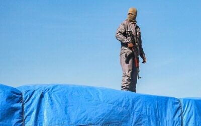 Un membre des forces de sécurité loyales au Hamas montant la garde sur l'un des camions transportant de l'aide humanitaire en provenance du poste-frontière de Kerem Shalom, à al-Shoka, à l'est de Rafah, dans le sud de la bande de Gaza, le 21 janvier 2025. (Crédit : Bashar Taleb/AFP)