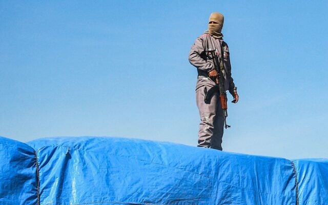 Un membre des forces de sécurité loyales au Hamas montant la garde sur l'un des camions transportant de l'aide humanitaire en provenance du poste-frontière de Kerem Shalom, à al-Shoka, à l'est de Rafah, dans le sud de la bande de Gaza, le 21 janvier 2025. (Crédit : Bashar Taleb/AFP)