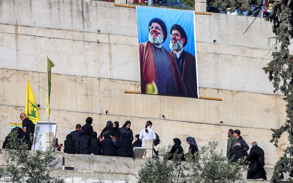 Une bannière affichant l'image des chefs du Hezbollah Hassan Nasrallah (à gauche) et de son successeur désigné Hashem Safieddine (à droite), au-dessus de personnes en deuil visitant les tombes des personnes tuées lors du conflit avec Israël dans le village de Kfarkila, au sud du Liban, près de la frontière avec Israël, le 31 mars 2025. (Rabih Daher/AFP).