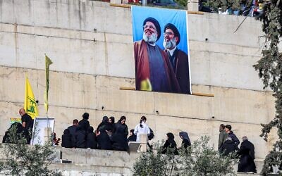 Une bannière affichant l'image des chefs du Hezbollah Hassan Nasrallah (à gauche) et de son successeur désigné Hashem Safieddine (à droite), au-dessus de personnes en deuil visitant les tombes des personnes tuées lors du conflit avec Israël dans le village de Kfarkila, au sud du Liban, près de la frontière avec Israël, le 31 mars 2025. (Rabih Daher/AFP).