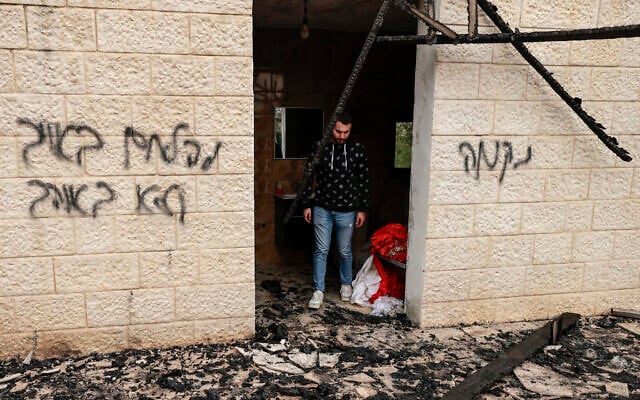 Un Palestinien passant devant des graffitis en hébreu : « Vengeance » (à droite), « Combattez l'ennemi, pas l'allié » (à gauche), dans un bâtiment après une attaque présumée de résidents d'implantations israéliens, dans la ville de Sadya à proximité de la ville de Salfit, en Cisjordanie, le 8 avril 2025. (Crédit : Jaafar Ashtiyeh/AFP)
