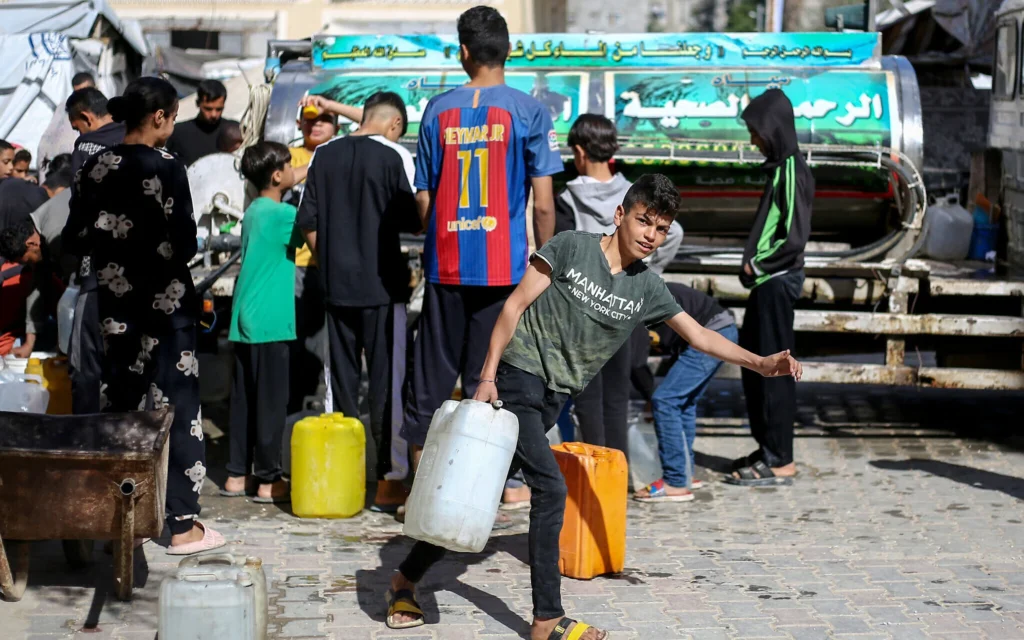 Des Palestiniens déplacés font la queue pour remplir leurs conteneurs d'eau au camp de réfugiés de Bureij, dans le centre de la bande de Gaza, le 10 avril 2025. (Crédit : Eyad BABA / AFP)