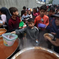 Des enfants palestiniens reçoivent leur part d'un repas chaud dans un point de distribution de nourriture gratuite dans le camp de réfugiés de Nuseirat, dans le centre de la bande de Gaza, le 12 avril 2025. (Crédit : Eyad BABA / AFP)