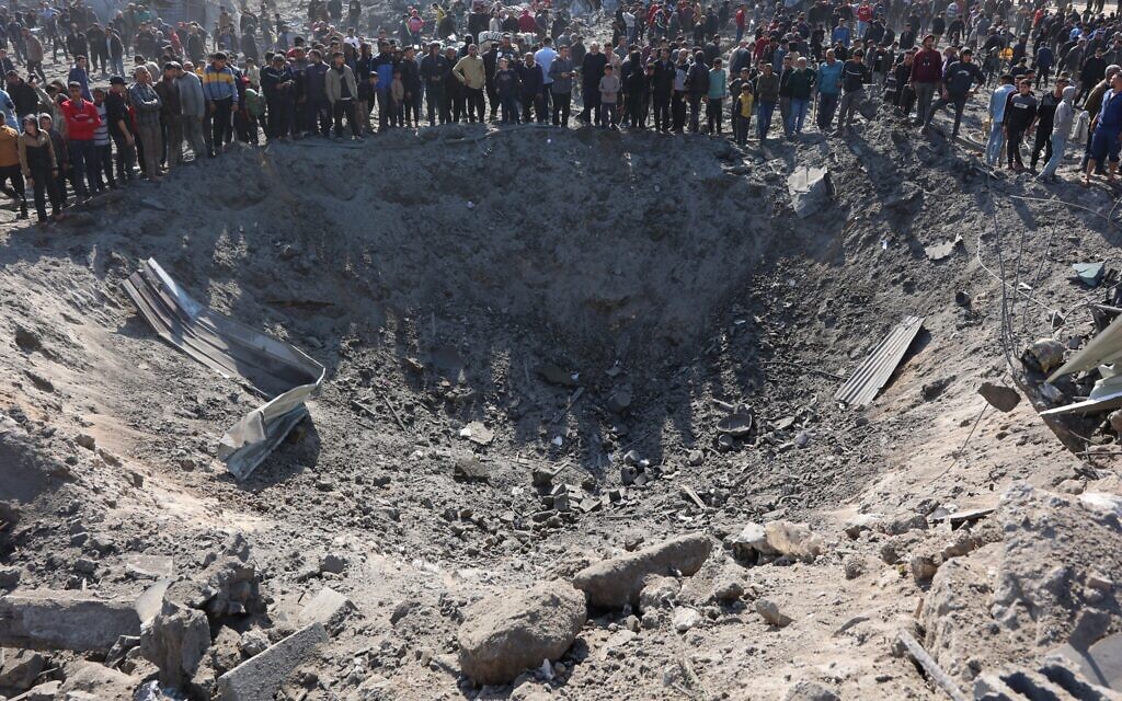 Des Palestiniens réunis autour d'un grand cratère suite à une frappe israélienne dans le quartier de Zaytoun, à Gaza, le 13 avril 2025. (Crédit : Omar Al-Qattaa/AFP)