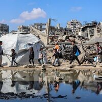 Des personnes passant près d'un abri de fortune érigé près des décombres d'un bâtiment effondré dans le quartier de Nasr, à l'ouest de la ville de Gaza, le 15 avril 2025. (Crédit : Omar Al-Qattaa/AFP)