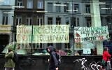 Des personnes passant devant des banderoles accrochées à l'intérieur d'une fenêtre d'un campement installé par des étudiants et des militants anti-Israël, à l'Université de Gand, alors que des étudiants occupent certaines parties du campus à Gand, en Belgique, le 16 mai 2024. (Crédit : Virginia Mayo/AP)