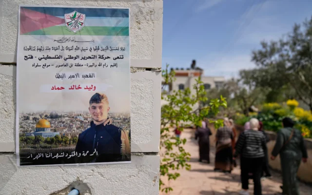 Des Palestiniennes passant devant une affiche représentant Walid Ahmad, sur laquelle on peut lire en arabe : "Le héros prisonnier martyr, la miséricorde et l'éternité pour nos justes martyrs", à Silwad, au nord-est de Ramallah, le 26 mars 2025. (Crédit : Nasser Nasser/AP)