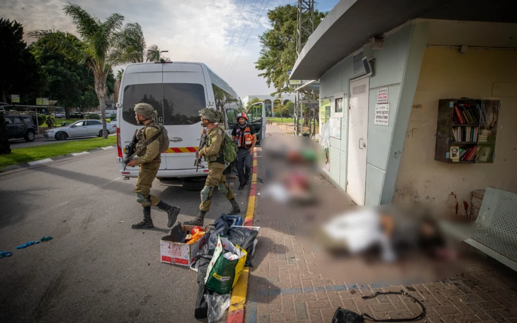 Des soldats israéliens marchent à côté des corps sans vie de personnes assassinées par des terroristes du Hamas, gisant à l'extérieur de l'abri dans la ville de Sderot, au sud d'Israël, le 7 octobre 2023. (Crédit :  Jamal Awad/Flash90)