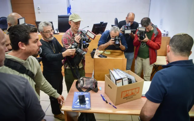 Des photographes prennent des photos d'une boîte de preuves présentée lors d'une audience au tribunal pour Jonatan Urich et Eli Feldstein qui ont été arrêtés dans le cadre de l'enquête sur le Qatargate, au tribunal de première instance de Rishon Lezion, le 1er avril 2025. (Crédit : Avshalom Sassoni/Flash90) Des photographes prennent des photos d'une boîte de preuves présentée lors d'une audience au tribunal pour Jonatan Urich et Eli Feldstein qui ont été arrêtés dans le cadre de l'enquête sur le Qatargate, au tribunal de première instance de Rishon Lezion, le 1er avril 2025. (Crédit : Avshalom Sassoni/Flash90)