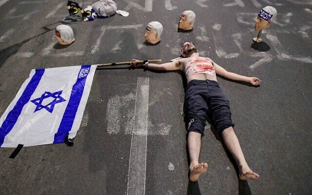 Une installation de masques représentant le visage du Premier ministre Benjamin Netanyahu entourant un manifestant allongé portant des bandages imbibés de faux sang lors d'une manifestation anti-gouvernement, à Tel Aviv, le 26 avril 2025. (Crédit : Tomer Neuberg/Flash90)
