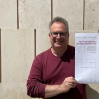 Doron Levy, chef du département de la langue des signes israélienne à l'Académie de la langue hébraïque, tenant une affiche expliquant les signes de base de la langue des signes israélienne, le 24 mars 2025. (Crédit : Rossella Tercatin/Times of Israel)