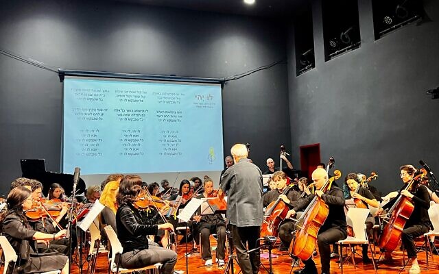 Le chef d'orchestre Michael Wolpe, avec l’ex-otage Agam Berger (au centre), se produisant avec l'Orchestre Lu Yehi, à Jérusalem, le 8 avril 2025. (Crédit : Autorisation)
