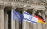 Le drapeau israélien flotte entre le drapeau européen (à gauche) et le drapeau allemand devant le bâtiment du Reichstag, siège du Bundestag, la chambre basse du Parlement allemand à Berlin, tandis que le chancelier allemande y prononce un discours sur le conflit entre Israël et le Hamas lors d'une session du Bundestag, le 12 octobre 2023. (Crédit : Odd Andersen/AFP)