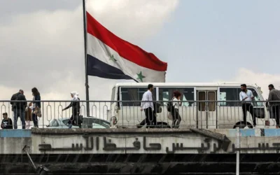 Un drapeau syrien flottant au vent tandis que des gens traversent le pont Hafez al-Assad, sur la rivière Barada, dans le centre de Damas, le 14 avril 2024. (Crédit : Louai Beshara/AFP)