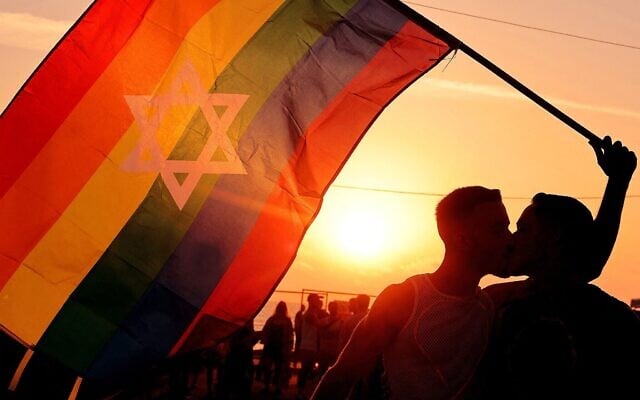 Deux hommes s'embrassent en tenant un drapeau arc-en-ciel au centre duquel se trouve une étoile de David à Tel Aviv, le 6 juin 2024. (Crédit : JACK GUEZ / AFP)