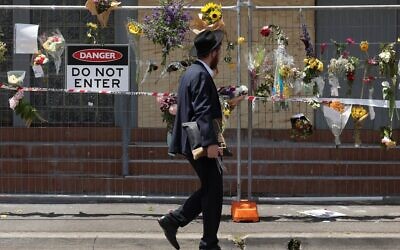 Un membre de la communauté juive lisant des messages accrochés à une clôture où des fleurs ont été déposées, à la synagogue Adass Israel, dans la banlieue de Ripponlea, à Melbourne, le 9 décembre 2024. (Crédit : Martin Keep/AFP)