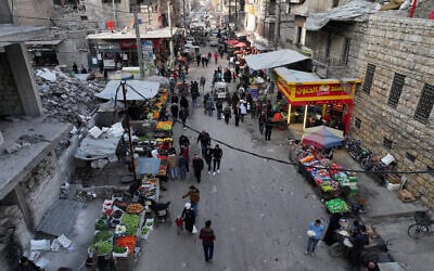 Des personnes marchant dans une rue commerçante bordée de bâtiments effondrés, détruits pendant la guerre civile syrienne, dans la ville d'Alep, au nord de la Syrie, le premier jour du ramadan, le 1ᵉʳ mars 2025. (Crédit : Omar Haj Kadour/AFP)