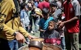 Des Palestiniens attendent devant un point de distribution de nourriture gratuite pour recevoir un repas chaud, dans le camp de réfugiés de Nuseirat, dans le centre de la bande de Gaza, le 19 avril 2025. (Crédit : Eyad BABA / AFP)