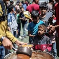 Des Palestiniens attendent devant un point de distribution de nourriture gratuite pour recevoir un repas chaud, dans le camp de réfugiés de Nuseirat, dans le centre de la bande de Gaza, le 19 avril 2025. (Crédit : Eyad BABA / AFP)