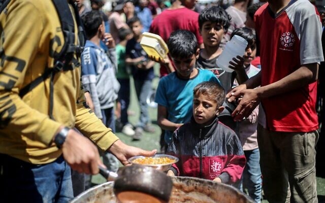 Des Palestiniens attendent devant un point de distribution de nourriture gratuite pour recevoir un repas chaud, dans le camp de réfugiés de Nuseirat, dans le centre de la bande de Gaza, le 19 avril 2025. (Crédit : Eyad BABA / AFP)