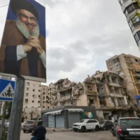 Dans le quartier de Ghobeiry, dans la banlieue sud de Beyrouth, des automobilistes passent devant des portraits du chef du Hezbollah libanais Hassan Nasrallah et des bâtiments endommagés par les frappes israéliennes lors de la récente guerre, à l'occasion du premier tour des élections municipales, le 4 mai 2025. (Crédit : ANWAR AMRO / AFP)