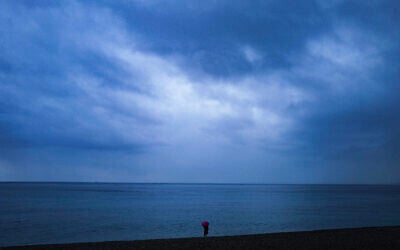 Une femme regarde la mer Méditerranée sous la pluie le long de la Promenade des Anglais sur la Côte d'Azur, à Nice, le 4 mai 2025. (crédit : Valery HACHE / AFP)