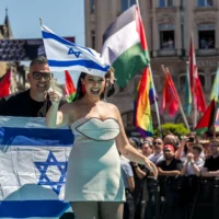 La chanteuse israélienne Yuval Raphael, représentant Israël avec la chanson « New Day Will Rise », marche sur le tapis turquoise à côté de l'hôtel de ville de Bâle, avec des drapeaux palestiniens de manifestants derrière, lors de la cérémonie d'ouverture du Concours Eurovision de la chanson 2025 à Bâle, le 11 mai 2025. (Crédit : Fabrice COFFRINI / AFP)