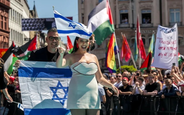 La chanteuse israélienne Yuval Raphael, représentant Israël avec la chanson « New Day Will Rise », marche sur le tapis turquoise à côté de l'hôtel de ville de Bâle, avec des drapeaux palestiniens de manifestants derrière, lors de la cérémonie d'ouverture du Concours Eurovision de la chanson 2025 à Bâle, le 11 mai 2025. (Crédit : Fabrice COFFRINI / AFP)