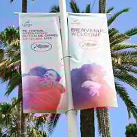 Une bannière annonçant le festival du film, près de palmiers, à la veille de la 78e édition du Festival de Cannes à Cannes, dans le sud de la France, le 12 mai 2025. (Crédit : Bertrand GUAY / AFP)