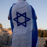 Avec le Dôme du Rocher à droite, un Israélien couvert d'un drapeau regarde des Israéliens brandir le drapeau national lors d'une parade organisée pour la Journée de Jérusalem dans la Vieille ville de Jérusalem, le 1er juin 2011. (Crédit : AP Photo/Ariel Schalit)
