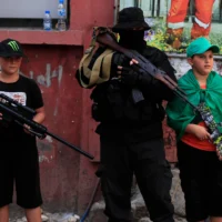 Un terroriste du Hamas, au centre, avec deux petits garçons se tiennent à côté de lui, avec des jouets de mitrailleuse  lors du cortège funèbre  d'un chef du Hamas, Samer al-Haj, qui a été tuépar une frappe de drone israélienne, au camp de réfugiés palestiniens Ein el-Hilweh, dans la ville portuaire méridionale de Sidon, le 10 août 2024. (Crédit : AP Photo/Mohammed Zaatari)