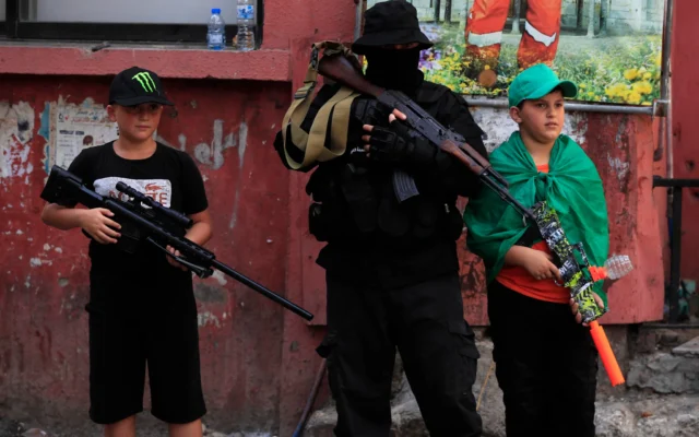 Un terroriste du Hamas, au centre, avec deux petits garçons se tiennent à côté de lui, avec des jouets de mitrailleuse  lors du cortège funèbre  d'un chef du Hamas, Samer al-Haj, qui a été tuépar une frappe de drone israélienne, au camp de réfugiés palestiniens Ein el-Hilweh, dans la ville portuaire méridionale de Sidon, le 10 août 2024. (Crédit : AP Photo/Mohammed Zaatari)