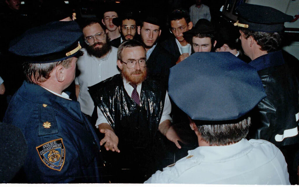 Des Juifs orthodoxes parlent avec la police du besoin de davantage de présence policière de façon à prévenir de nouvelles violences lors des émeutes anti-juives dans le quartier de Crown Heights, à Brooklyn, dans l'Etat de New York, le 21 août 1991. (Crédit : AP Photo/Andrew Savulich) Des Juifs orthodoxes parlent avec la police du besoin de davantage de présence policière de façon à prévenir de nouvelles violences lors des émeutes anti-juives dans le quartier de Crown Heights, à Brooklyn, dans l'Etat de New York, le 21 août 1991. (Crédit : AP Photo/Andrew Savulich)