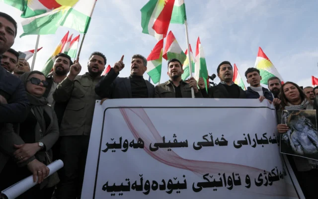 Des manifestants, au lendemain de frappes de missiles lancées par les Gardiens de la révolution iraniens sur plusieurs sites de la ville, brandissent une bannière et des drapeaux kurdes devant le bureau des Nations unies à Erbil, dans la région autonome kurde d’Irak, le 16 janvier 2024. (Crédit : Safin HAMID / AFP)