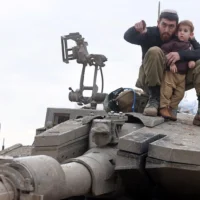 Un soldat israélien, son épouse  et leur enfant assis sur un char lors d'une visite familiale à son retour de mission dans la bande de Gaza, le 28 janvier 2024. (Crédit : Menahem KAHANA / AFP)