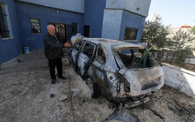 Un résident palestinien de Bruqin en Cisjordanie se tient à côté d'une voiture incendiée lors d'une attaque de partisans du mouvement pro-implantation israéliens, le 23 mai 2025. (Crédit : Jaafar Ashtiyeh / AFP