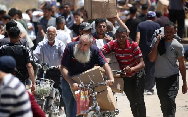 Des personnes transportent des caisses de fournitures de secours de la Fondation humanitaire de Gaza (GHF), un groupe d'aide privé soutenu par les Etats-Unis qui a contourné le système de longue date dirigé par l'ONU dans le territoire, alors que des Palestiniens déplacés reviennent d'un centre de distribution d'aide dans le centre de la bande de Gaza, le 29 mai 2025. (Crédit : Eyad BABA / AFP Des personnes transportent des caisses de fournitures de secours de la Fondation humanitaire de Gaza (GHF), un groupe d'aide privé soutenu par les Etats-Unis qui a contourné le système de longue date dirigé par l'ONU dans le territoire, alors que des Palestiniens déplacés reviennent d'un centre de distribution d'aide dans le centre de la bande de Gaza, le 29 mai 2025. (Crédit : Eyad BABA / AFP