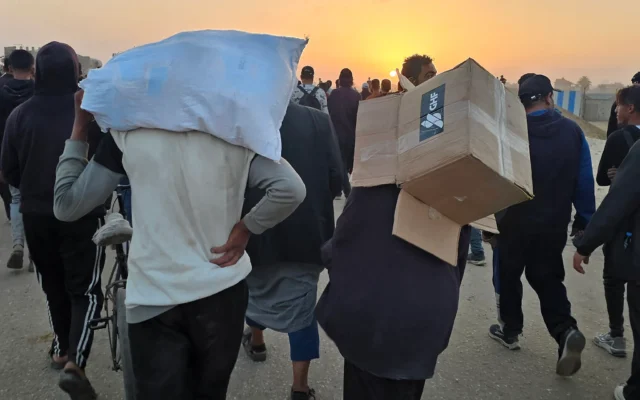 Un jeune portant une boîte vide de fournitures humanitaires provenant de la Gaza Humanitarian Foundation, tandis que des Palestiniens déplacés marchent près d'un centre de distribution alimentaire, à Rafah, dans le sud de la bande de Gaza, le 1ᵉʳ juin 2025. (Crédit : AFP) Un jeune portant une boîte vide de fournitures humanitaires provenant de la Gaza Humanitarian Foundation, tandis que des Palestiniens déplacés marchent près d'un centre de distribution alimentaire, à Rafah, dans le sud de la bande de Gaza, le 1ᵉʳ juin 2025. (Crédit : AFP)